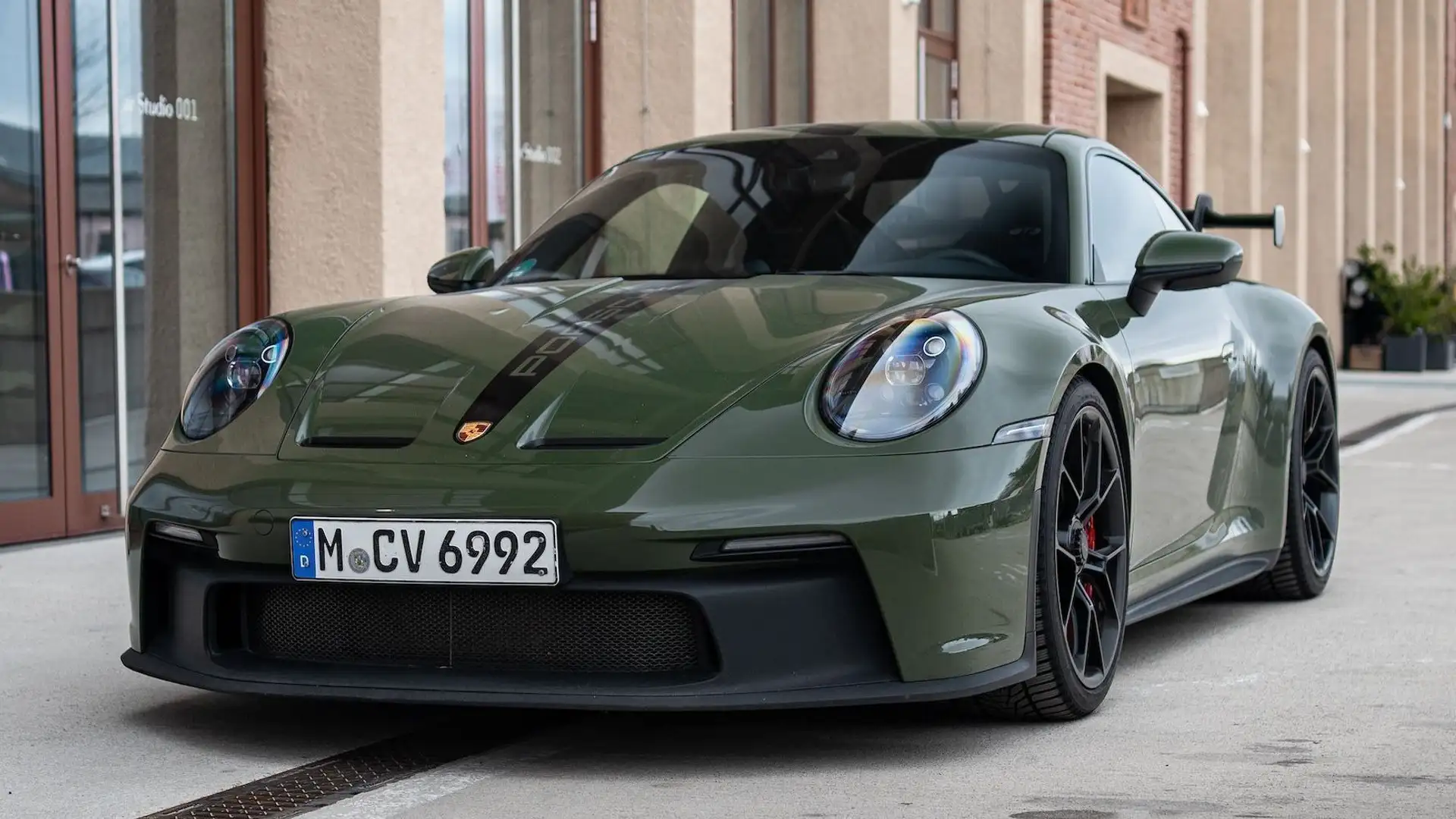 Our olive green Porsche GT3 photographed from the front in front of an industrial building.
